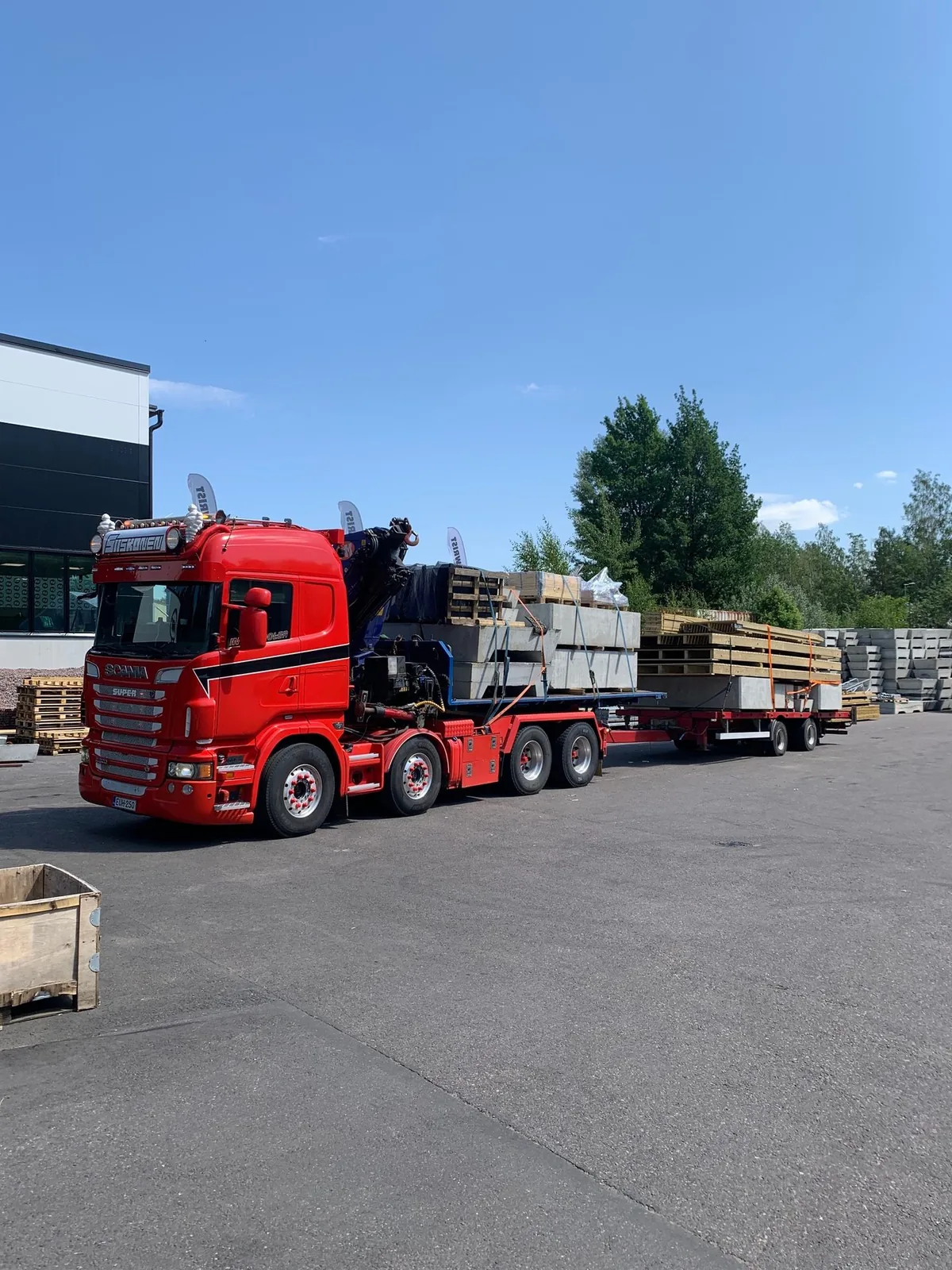 Punainen Scania R620 betonielementtien ja puutavaran kanssa varastopihalla.