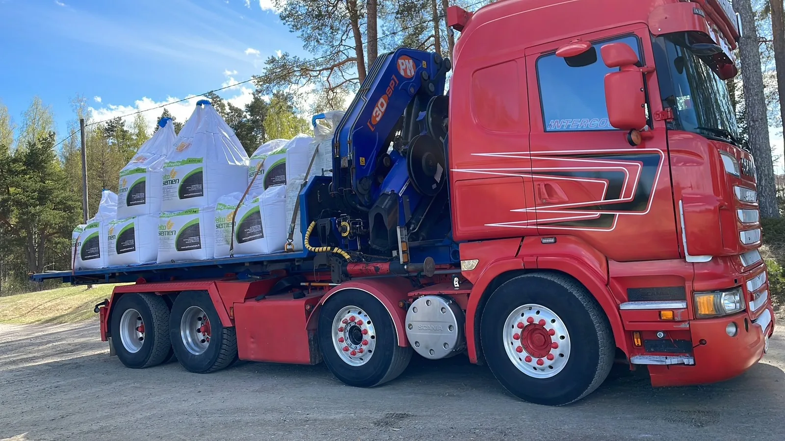 Punainen Scania ja suursäkkikuorma avolavalla, nosturi ohjaamon takana.