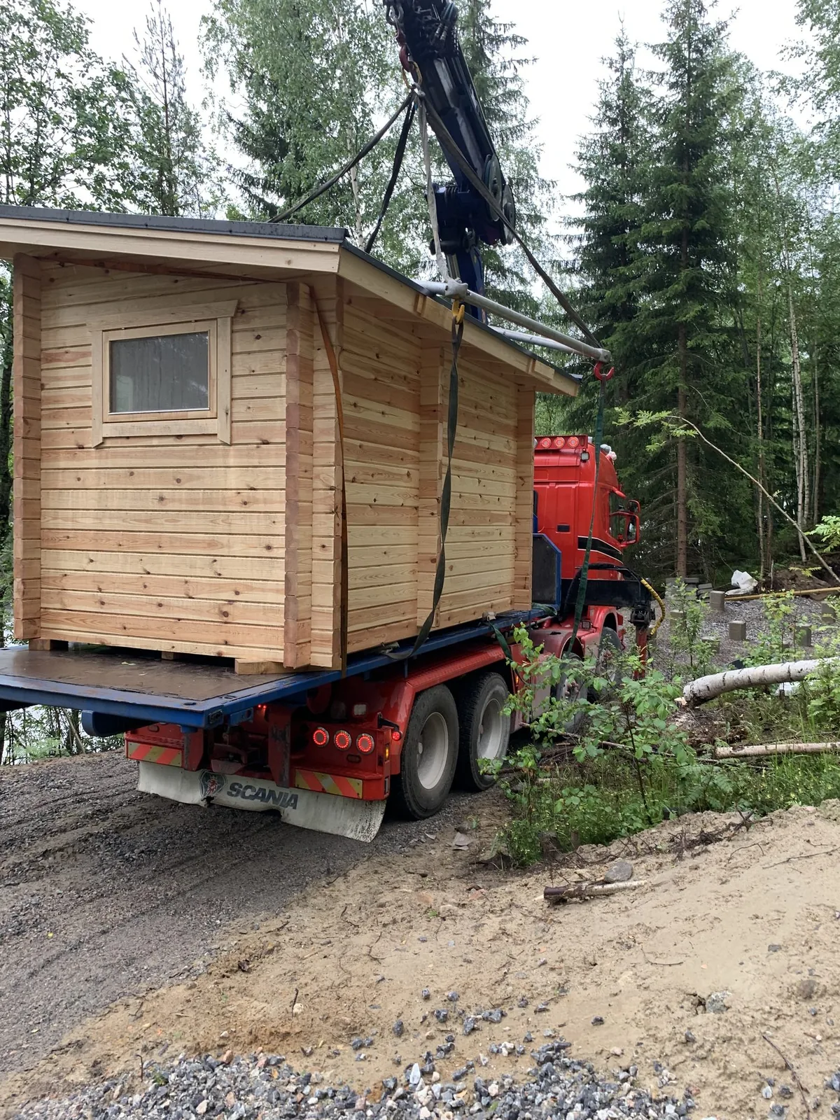 Hirsinen pihasauna nosturiauton lavalla, nostoliinat vielä kiinni.